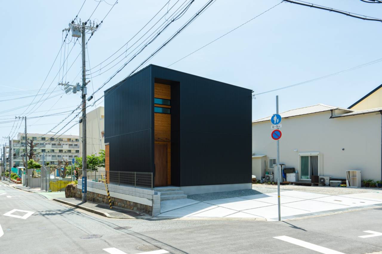石垣にそびえる黒と、空へ開くウッドデッキの家。